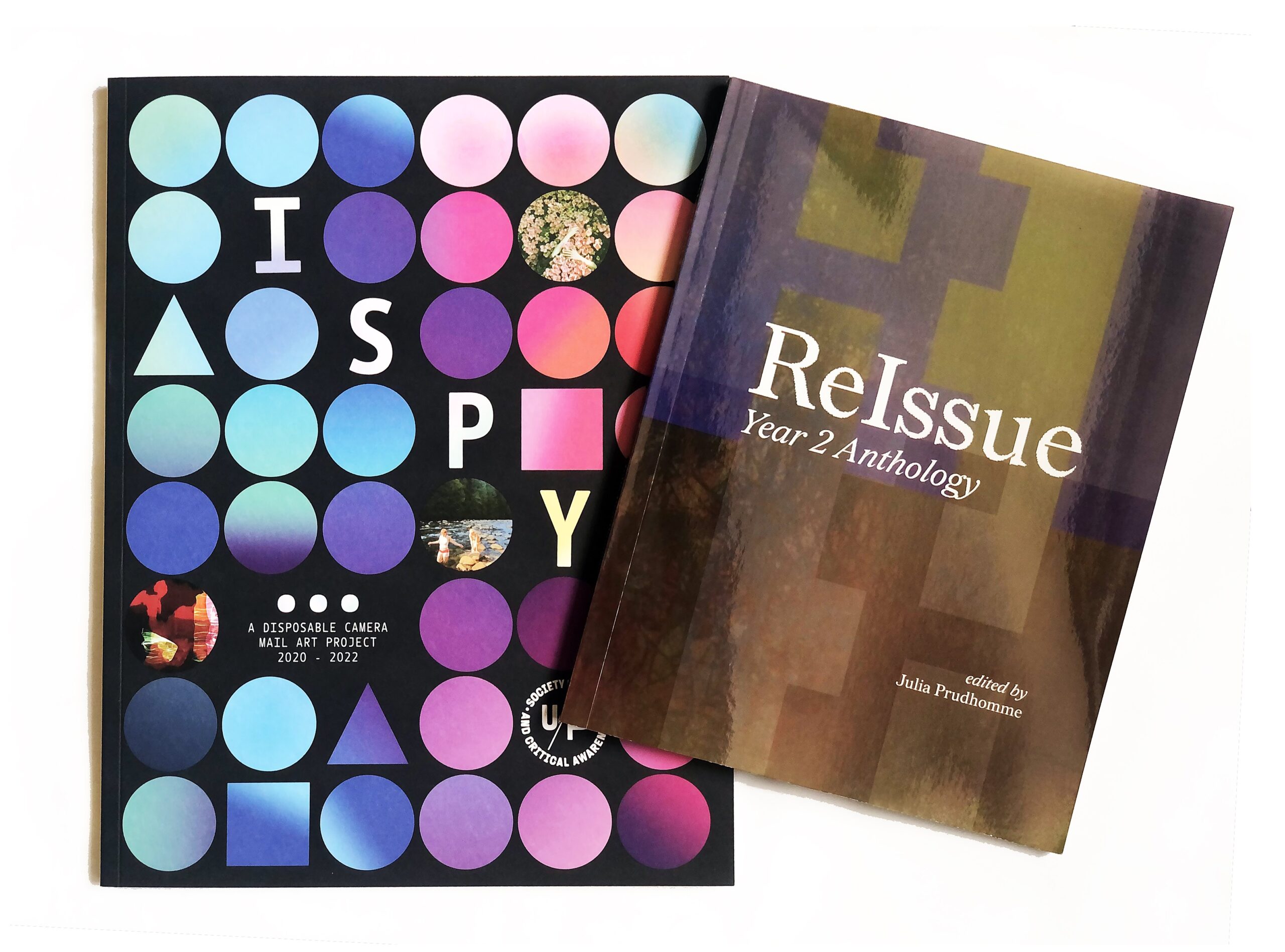 Two publications on a white background. I SPY catalogue has blue and pink dots in a grid form on a black background. ReIssue Year 2 Anthology has white text on an abstract green, purple, and brown background.