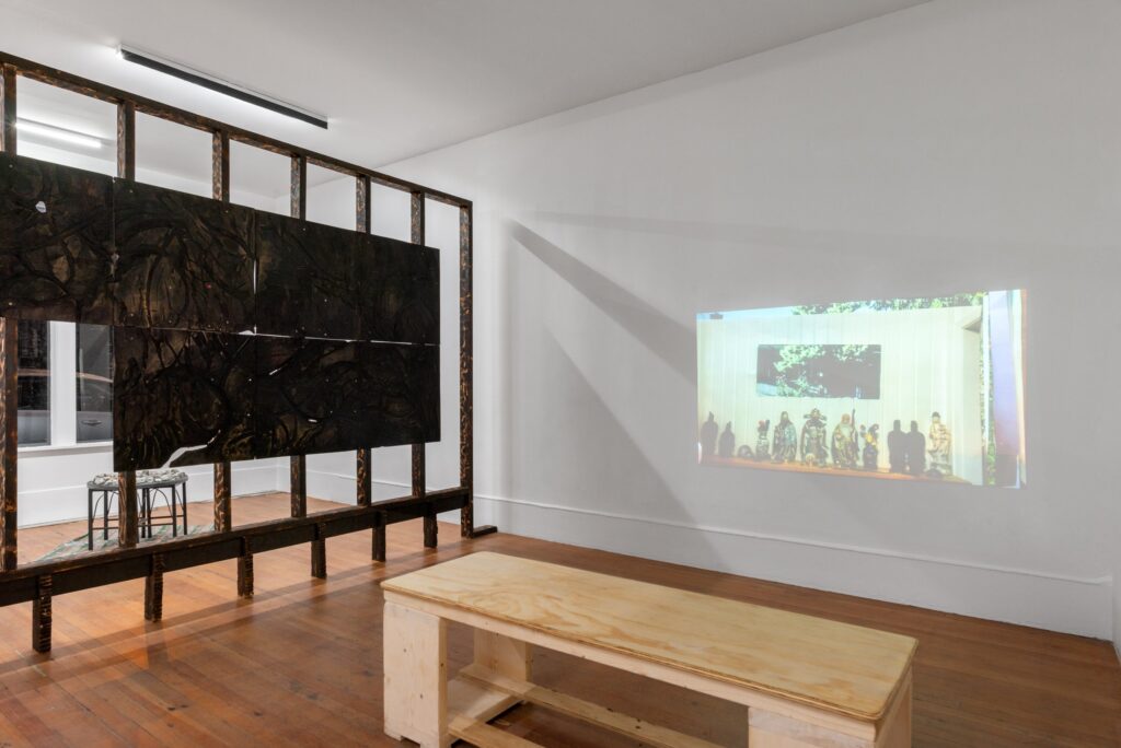 Installation image of Kiyoshi Whitley's work 'days; featuring a blackened piece of plywood, with carved linear forms, chalk, linseed oil, and designs burned onto the surface with a propane torch.