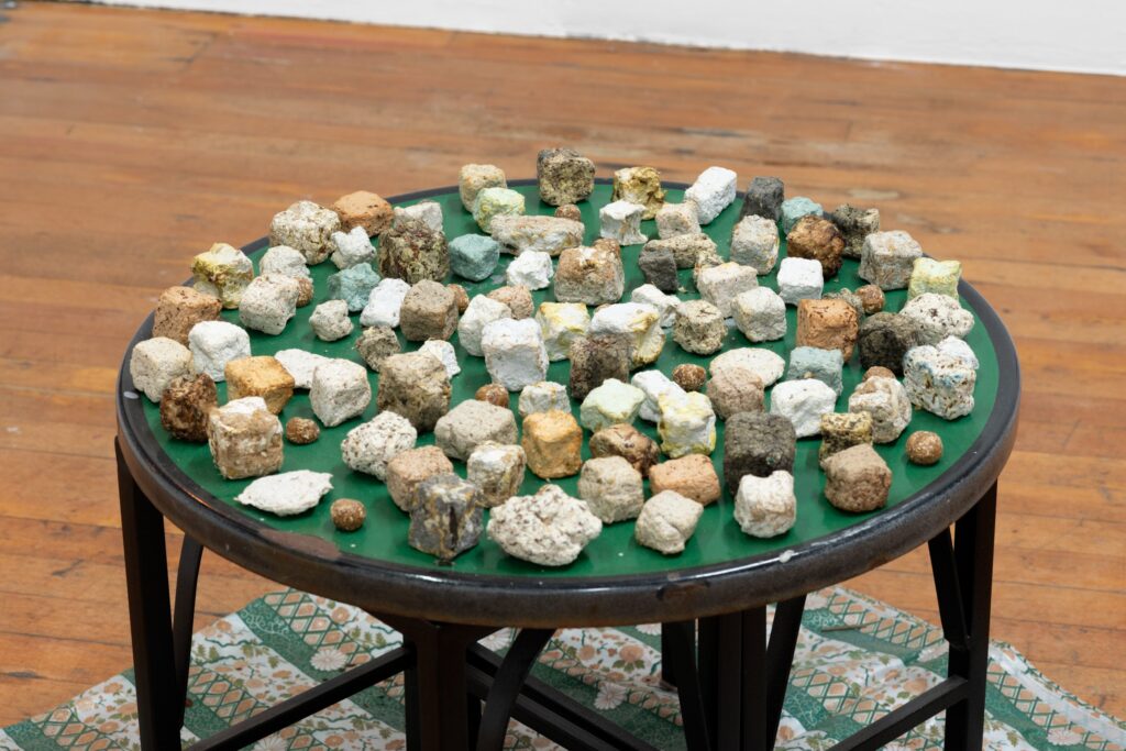 Detail of Sauha Lee's work featuring what she calls "chunks" of paper and foudn materials, which look like stone cubes. Placed on a round green table surface.