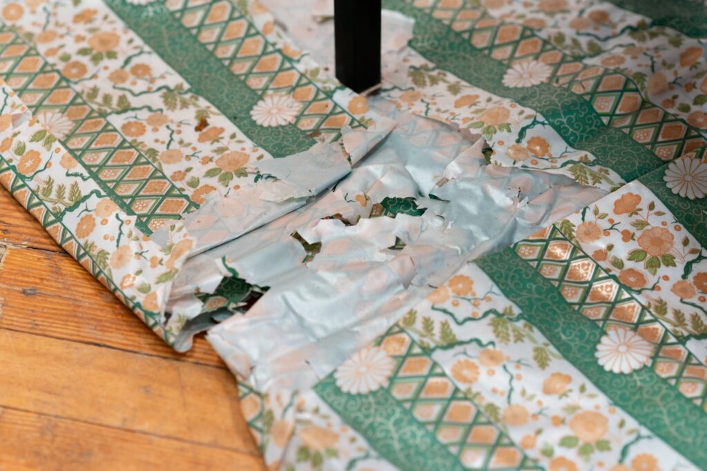 Detail of Sauha Lee's work showing the plastic cloth on which the sculpture sits—a green and gold floral design which is worn and falling apart from being left outside in the elements for too long.