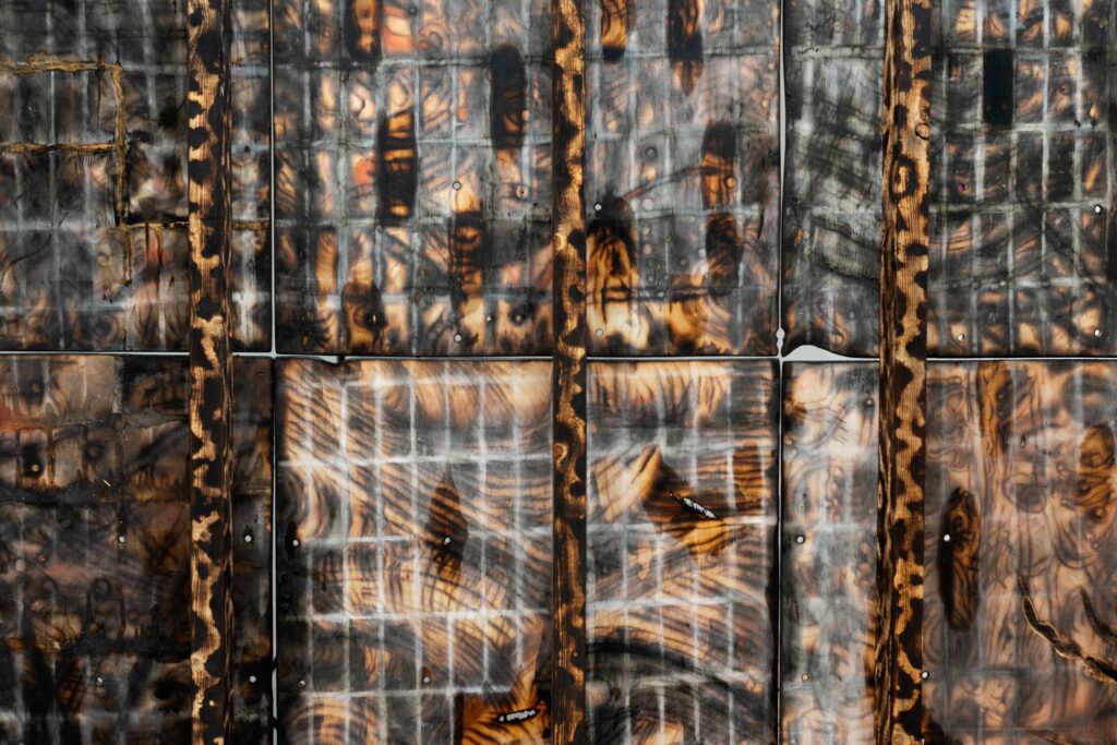 Detail image of Kiyoshi Whitley's work 'days; featuring a blackened piece of plywood, with carved linear forms, chalk, linseed oil, and designs burned onto the surface with a propane torch.