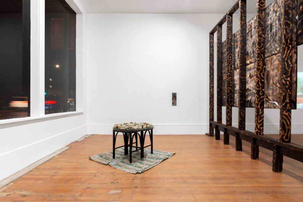 Installation view Sauha Lee's work featuring what she calls "chunks" of paper and foudn materials, which look like stone cubes. Placed on a round green table surface. Collage by Alyson Bucharest in the background, as well as Kiyoshi Whitley's installed sculpture.